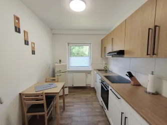 Eine moderne Küche mit Holzschränken und hellen Fliesen. Ein Tisch mit Stühlen steht neben einem Fenster.