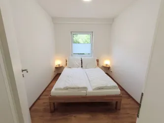 Ein einfaches Schlafzimmer mit einem Doppelbett und zwei Nachttischen. Es gibt ein Fenster, das Tageslicht hereinlässt.