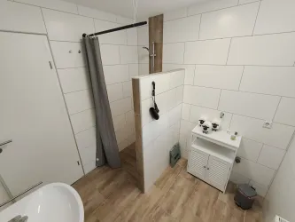 Ein modernes Badezimmer mit einer Duschkabine und Holzdekor. Auf der rechten Seite befindet sich ein kleiner Tisch mit Toilettenartikeln.