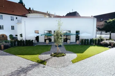 Ein modernes Gebäude mit weißen Wänden und großen Fenstern. Der Außenbereich ist mit einer grünen Rasenfläche und Schirmen ausgestattet.