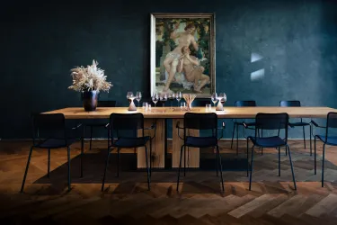 Ein eleganter Tisch aus Holz mit schwarzen Stühlen steht in einem stilvollen Raum. An der Wand hängt ein Kunstwerk, und der Tisch ist mit Gläsern dekoriert.