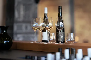 Eine stilvolle Anordnung von Weingläsern und Flaschen auf einer Holzoberfläche. Im Hintergrund sind weitere dekorative Elemente zu sehen.