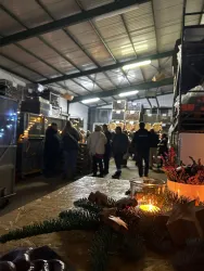 Ein lebhafter Innenraum mit vielen Menschen, die in einem Lager stehen. Auf einem Tisch im Vordergrund sind Kerzen und dekoratives Grün zu sehen.