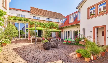 Ein einladender Innenhof mit begrünten Pflanzkübeln und Terrassenmöbeln. Sonnenschirme sorgen für Schatten und eine gemütliche Atmosphäre.