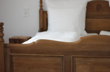 Ein rustikales Holzbett mit weißen Kissen und Decke. Neben dem Bett steht ein kleiner Holzstuhl.