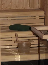 Eine Sauna mit hölzernen Bänken, einem grünen Handtuch und einem Eimer aus Holz. Die Atmosphäre ist entspannend und einladend.