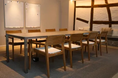 Ein eleganter Besprechungsraum mit einem langen Tisch und Holzstühlen. An der Wand befinden sich zwei Flipcharts.