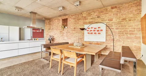 Ein modernes Esszimmer mit einer Holztischplatte und eleganten Stühlen. Die Wände sind aus rotem Stein und die Küche ist offen gestaltet.