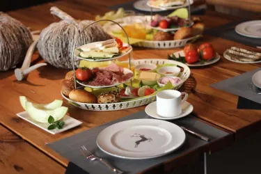 Ein liebevoll angerichtetes Frühstücksbuffet mit verschiedenen Käsesorten, Aufschnitt, frischem Obst und Brötchen. Die Tafel ist elegant dekoriert, ideal für einen gemütlichen Start in den Tag.