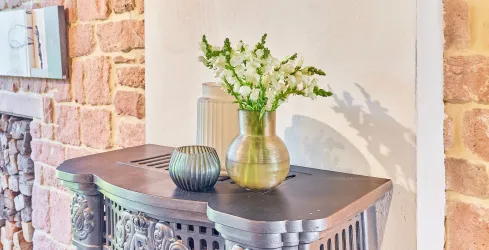 Eine dekorative Kommode mit einem Blumenstrauß in einer Vase und einer weiteren kleinen Vase. Im Hintergrund sind steinerne Wände zu sehen.