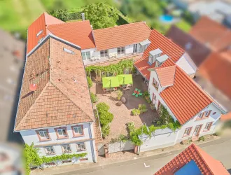 Eine schöne Ansicht eines Gebäudekomplexes mit roten Dächern und einem Innenhof. Der Innenhof ist mit Pflanzen und Gartenmöbeln ausgestattet und lädt zum Verweilen ein.