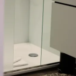 Eine moderne Dusche mit Glasabtrennung und einem weißen Duschboden. Zwei Handtücher liegen auf dem Boden.