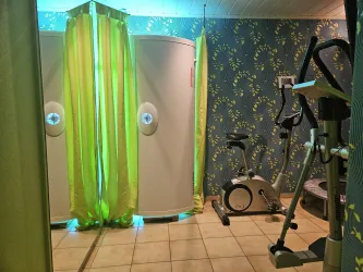 Ein Raum mit zwei grünen Vorhängen und zwei Kabinen. Auf der linken Seite steht ein Fitnessgerät.