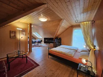 Ein gemütliches Schlafzimmer mit Holzdecke und einem Doppelbett. Der Raum hat einen Tisch, Stühle und viel Tageslicht.