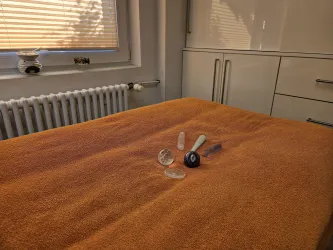 Ein orangefarbener Bettüberwurf mit mehreren kosmetischen Flaschen und Behältern darauf. Im Hintergrund ist ein Fenster mit natürlichem Licht sichtbar.
