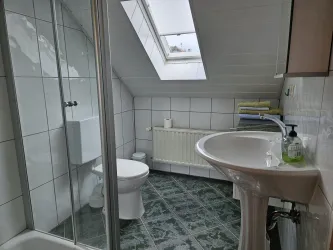 Ein modernes Badezimmer mit Dusche, Waschbecken und WC. Es hat helle Fliesen und ein Dachfenster für natürliches Licht.