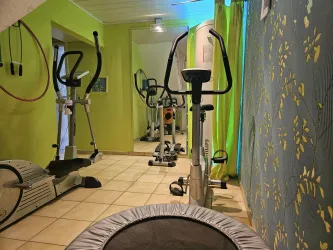 Ein funktioneller Fitnessraum mit verschiedenen Trainingsgeräten. Die Wände sind in einem lebhaften Grünton gehalten, und es gibt einen Trampolin im Vordergrund.