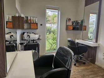 Ein modernes Friseurstudio mit zwei Stühlen und großen Spiegeln. Der Raum hat Fenster, die Licht und eine grüne Aussicht bieten.