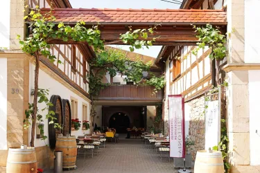 Ein malerischer Innenhof mit einer Holzverkettung und üppigem Pflanzenbewuchs. Tische und Stühle laden zum Verweilen ein.