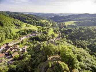 Eine wunderschöne Landschaft mit grünen Hügeln und bewaldeten Bereichen. Im Vordergrund sind kleine Häuser zu sehen, die sich harmonisch in die Natur einfügen.