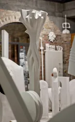 Eine kreative Skulptur in einem Atelier mit verschiedenen weißen Objekten. Im Hintergrund sind Ziegelwände und weitere Kunstwerke sichtbar.