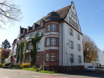 Ein historisches Gebäude mit einem charmanten Dach und Fenstern. Es ist von Bäume und Grünflächen umgeben.