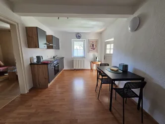 Eine moderne Küche mit Holzschränken und einem kleinen Essbereich. Der Raum ist hell und freundlich, mit viel natürlichem Licht.