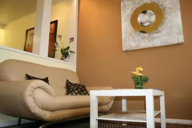 Ein gemütliches Wohnzimmer mit einem beigen Sofa und einem kleinen weißen Tisch. An der Wand hängt ein modernes Kunstwerk und eine Pflanze steht in der Ecke.