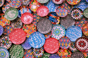 Bunte, handgefertigte Teller mit verschiedenen geometrischen Mustern sind übereinander gestapelt. Die Farben sind lebhaft und vielfältig.