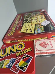 Eine Sammlung von Spielen, darunter ein großes Spielset und ein UNO-Spiel. Daneben liegt ein Kartenspiel.