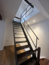 Eine moderne Treppe aus Holz und Metall führt nach oben. Das Licht kommt durch ein Fenster an der Decke.