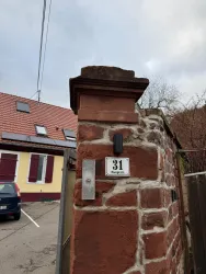 Ein historisches Tor mit einer Wettersteiner-Mauer und einer Hausnummer 31. Im Hintergrund sind ein paar Häuser und eine graue Wolkendecke zu sehen.