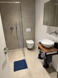 Ein modernes Badezimmer mit einer Duschkabine und einem stilvollen Waschbecken. Der Boden ist hell gefliest und es gibt eine blaue Badematte.