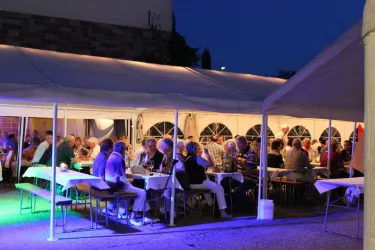 <p>Eine festliche Veranstaltung unter einem Zelt am Abend. Viele Gäste sitzen an Tischen und genießen das Beisammensein.</p>