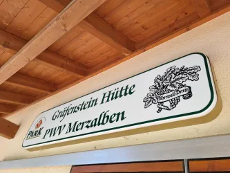 Ein Schild mit der Aufschrift "Grafenstein Hütte PWV Merzalben". Es befindet sich unter einem Holzdach und ist gut sichtbar.