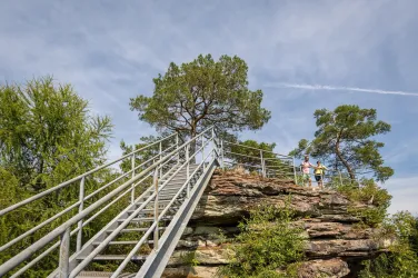 Eine Aussichtsplattform auf einem Felsen mit einer Treppe. Zwei Personen stehen oben und genießen die Aussicht.