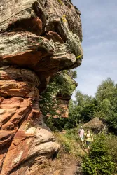 Zwei Wanderer erkunden einen schmalen Pfad zwischen beeindruckenden Felsformationen. Die Umgebung ist grün und sonnig, ideal für Outdoor-Aktivitäten.
