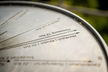 Eine Metalltafel mit Entfernungsangaben zu verschiedenen Orten. Die Inschriften sind gut lesbar und zeigen die Richtung und Distanz zu den jeweiligen Zielen.