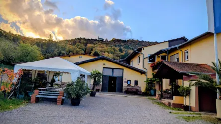 Ein einladendes Gebäude in ländlicher Umgebung mit einem Gartenbereich und einem Zelt. Die Landschaft im Hintergrund zeigt Hügel und einen schönen Himmel.