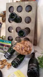 Ein stilvolles Weinregal aus Holz mit mehreren Weinflaschen und Korken. Im Vordergrund sind einige Korken und eine Broschüre sichtbar.