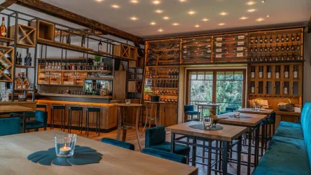 Ein gemütliches Restaurant mit Holzregalen, die eine Auswahl an Getränken zeigen. Die Einrichtung ist modern und einladend, mit Barhockern und Tischen.