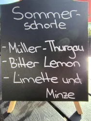Ein Schild mit der Aufschrift „Sommer-schorle“. Es listet die Zutaten: Müller-Thurgau, Bitter Lemon und Limette und Minze.
