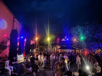 Ein lebhaftes Nachtleben mit vielen Menschen in einem Außenbereich. Bunte Lichter erhellen die Szene und schaffen eine festliche Atmosphäre.
