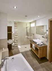 Ein modernes Badezimmer mit einer Dusche und einer Badewanne. Helle Wandfliesen und Holzakzente schaffen eine elegante Atmosphäre.