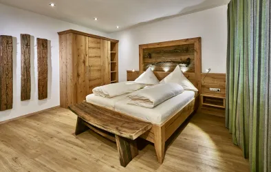 Ein modernes Schlafzimmer mit einem großen Holzbett und zwei Kissen. Die Wände sind hell, und es gibt Holzregale sowie Vorhänge in Grün.