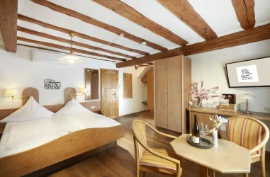 Ein gemütliches Hotelzimmer mit Holzbalken und modernen Möbeln. Es gibt ein Doppelbett, einen Tisch und einen Fernseher.