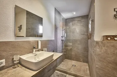 Ein modernes Badezimmer mit einer ebenerdigen Dusche und einem eleganten Waschbecken. Die Wände sind mit braunen Fliesen gestaltet, die eine schlichte und stilvolle Atmosphäre schaffen.