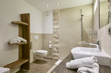 Ein modernes Badezimmer mit einer eleganten Dusche und einem Waschbecken. Holzregale und frische Handtücher verleihen dem Raum eine einladende Atmosphäre.