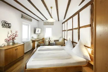Ein gemütliches Zimmer mit einem Doppelbett und Holzdecken. Es gibt einen Schreibtisch, einen Fernseher und natürliche Lichtquellen.