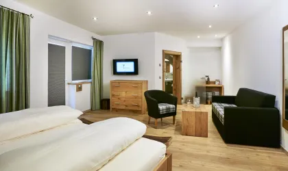 Ein modernes Hotelzimmer mit zwei Betten, einem Fernseher und gemütlicher Sitzecke. Große Fenster lassen viel Licht herein und die Einrichtung ist schlicht und stilvoll.